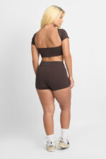 Short Ema Cacau: Conjunto de treino marrom com top cropped e shorts, meias brancas e tênis.