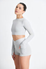 Mulher vestindo Short Yani Lunar cinza e top de manga comprida. Roupa de treino confortável.