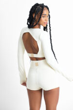 Short Yani Macadâmia: Conjunto atlético cor creme com top cropped de manga longa e shorts combinando, com detalhe recortado nas costas.