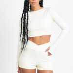 Mulher vestindo SHORT YANI MACADÂMIA cor creme, top cropped de manga comprida e shorts combinando.