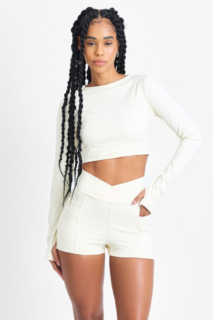 Mulher vestindo SHORT YANI MACADÂMIA cor creme, top cropped de manga comprida e shorts combinando.