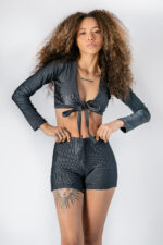 Mulher com top e shorts pretos, cabelo cacheado. Tatuagens visíveis.