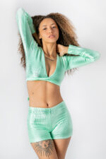 Modelo em conjunto verde água canelado: top cropped e shorts. Cabelos cacheados e tatuagens.